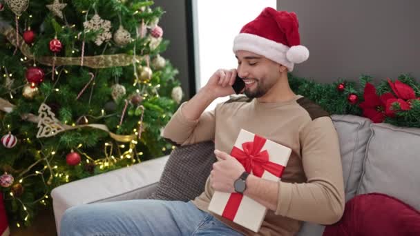 年轻的Arab男子拿着礼物坐在圣诞树旁坐在家里用智能手机交谈 — 图库视频影像
