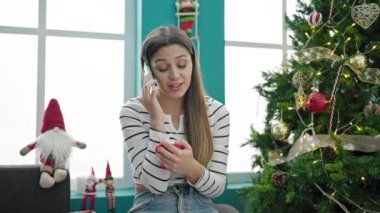 Mutlu genç kız sıcak içecek içiyor ve evde Noel 'i kutlarken cep telefonuyla konuşuyor.  