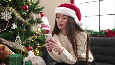 Güzel genç bir kadın Noel 'i kutluyor ve evde akıllı telefon kullanıyor.