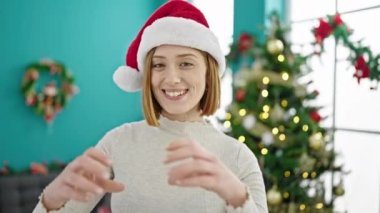 Evdeki Noel ağacının önünde gülümseyen genç sarışın kadın.