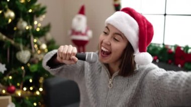 Evdeki Noel ağacının yanında mikrofonla şarkı söyleyen güzel İspanyol bir kadın.
