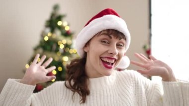 Kırmızı kazaklı ve Noel Baba şapkalı mutlu genç kadın Noel arifesinde evde dans ediyor, Noel 'i ve yeni yılı kutluyor..