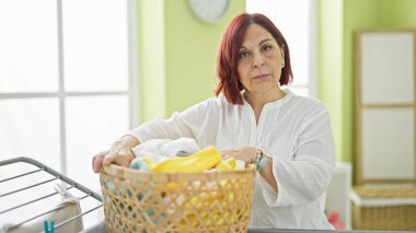 Çamaşır odasında elinde sepet tutan orta yaşlı bir kadın.