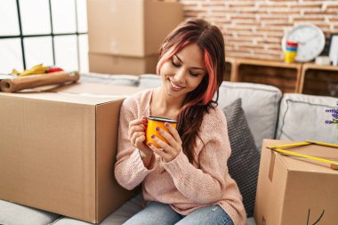 Yeni evindeki kanepede kahve içen beyaz bir kadın.