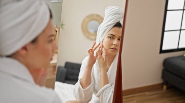 Bornoz giymiş genç ve güzel bir İspanyol kadın yatak odasındaki aynaya bakıyor.