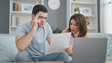 Evdeki kanepede oturmuş dizüstü bilgisayar okuyan güzel bir çift.