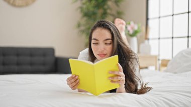 Genç, güzel, İspanyol bir kadın yatak odasında kitap okuyor.