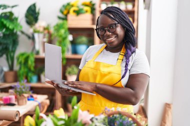 Çiçekçiye dizüstü bilgisayar kullanarak gülümseyen Afrikalı Amerikalı kadın.