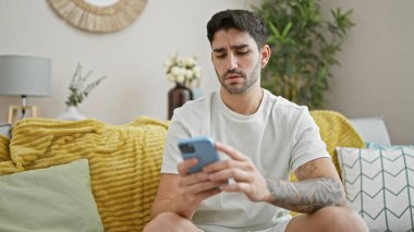 Evdeki kanepede oturan, akıllı telefon kullanan genç bir İspanyol.