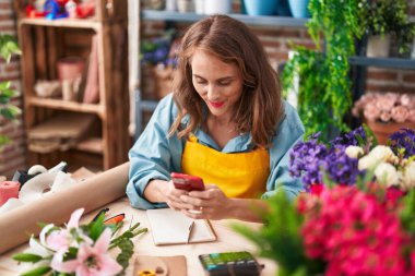 Çiçekçiye akıllı telefon kullanarak gülümseyen güzel İspanyol kadın.