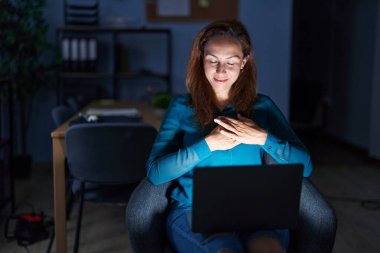 Geceleri ofiste çalışan esmer bir kadın elleri göğsünde, gözleri kapalı ve yüzünde minnet dolu bir jest ile gülümsüyor. sağlık kavramı. 