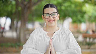 Genç, güzel İspanyol kadın parkta dua ederken gülümsüyor.