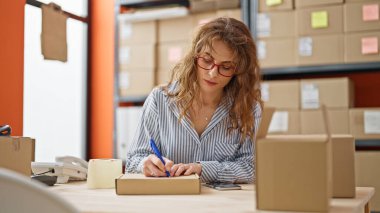 Genç kadın ecommerce iş işçisi ofiste paket üzerine yazıyor.