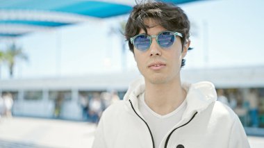 Parkta güneş gözlüğü takan, ciddi bir suratı olan genç bir İspanyol.