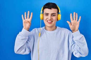 İkili olmayan kişi kulaklık kullanarak müzik dinliyor dokuz numaralı parmaklarıyla gösterip işaret ederken kendinden emin ve mutlu gülümsüyor.. 