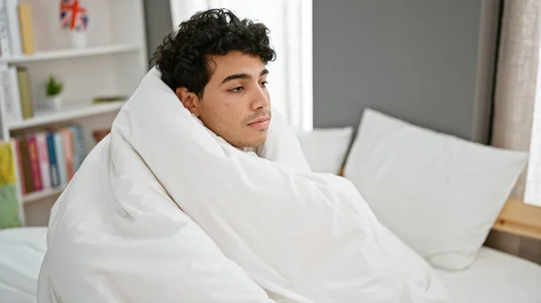 Young latin man covering with blanket at bedroom
