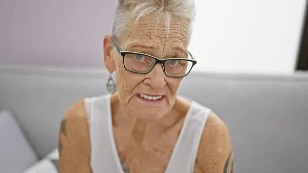 Przytulnym Domu Dojrzała Siwowłosy Kobieta Okularach Wykazuje Poważny Wyraz Twarzy — Zdjęcie stockowe