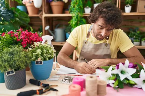 Young hispanic man florist writing on notebook at flower shop
