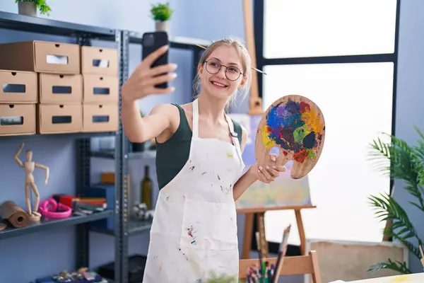 年轻的高加索女艺术家微笑着自信地通过智能手机在艺术工作室里自拍 — 图库照片