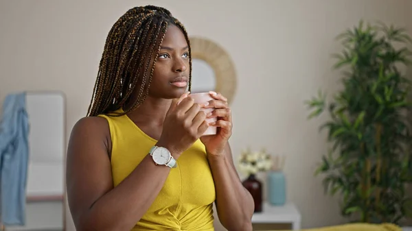 African american woman drinking coffee standing with serious face at home