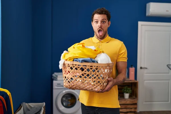 Young Hispanic Man Holding Laundry Basket Afraid Shocked Surprise Amazed — Fotografia de Stock