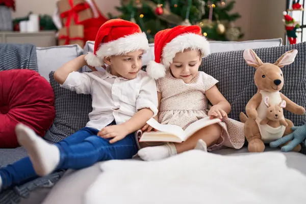 Δύο Παιδιά Διαβάζουν Βιβλίο Κάθεται Στον Καναπέ Από Χριστουγεννιάτικο Δέντρο — Φωτογραφία Αρχείου