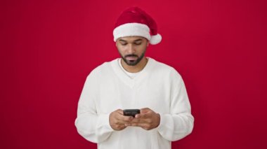 Kırmızı Noel Baba şapkalı mutlu Noel Baba 'nın portresi kırmızı arka planda akıllı telefon kullanıyor.
