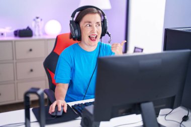 Orta yaşlı İspanyol kadın video oyunları oynuyor başparmağıyla yan tarafı işaret ediyor ve ağzı açık gülümsüyor. 