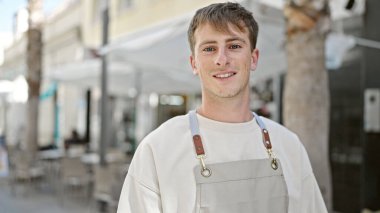 Kafkasyalı genç garson, kahvecinin terasında kendine güvenen bir şekilde gülümsüyor.