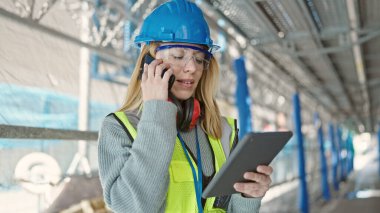 Sarışın bir müteahhit, dokunmatik ped kullanıyor ve akıllı telefondan konuşuyor.