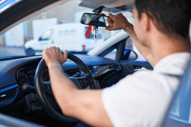 Latin kökenli genç adam dikiz aynasına dokunuyor. Sokakta arabada oturuyor.