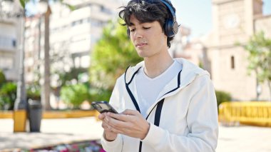 Genç İspanyol adam parkta müzik dinliyor.