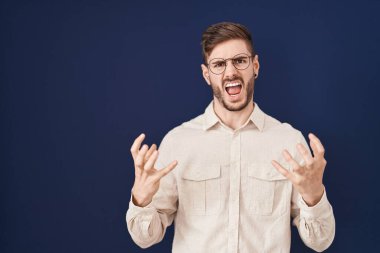 Mavi arka planda sakallı İspanyol bir adam. Deli gibi bağırıyor, agresif bir ifadeyle bağırıyor ve kollarını kaldırıyor. hüsran kavramı. 