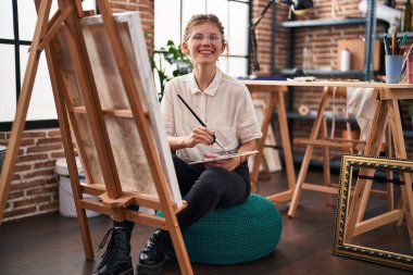 Sanat stüdyosunda kendine güvenen genç sarışın sanatçı gülümsüyor.