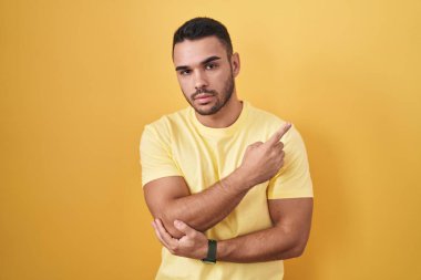 Sarı arka planda dikilen genç İspanyol adam, el ile işaret ederek reklamını yapıyor, ciddi ve sakin bir yüz ifadesi. 