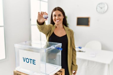 Young beautiful hispanic woman electoral table president holding vote badge at electoral college