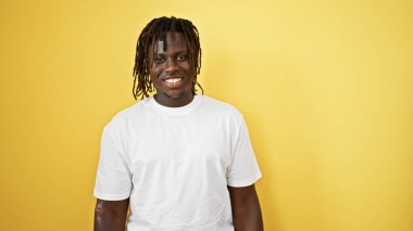 Afro-Amerikalı bir adam, kendinden emin bir şekilde, izole edilmiş sarı arka planda duruyor.