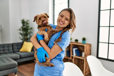 Young beautiful hispanic woman veterinarian smiling confident hugging dog at home