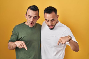 Sarı arka planda dikilen eşcinsel çift parmaklarını göstererek reklamını yapıyor, şaşırmış yüz ve ağzını açıyor. 