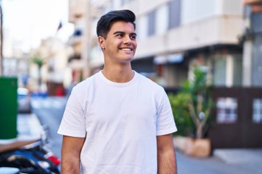 Young hispanic man smiling confident looking to the side at street