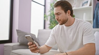 Evdeki kanepede oturan, akıllı telefon kullanan genç bir İspanyol.