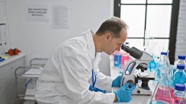 Laboratuvarda mikroskop kullanan orta yaşlı bilim adamı.