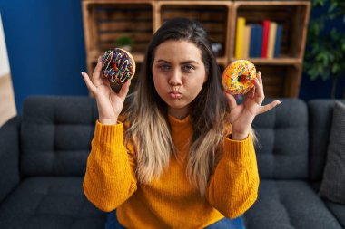 Genç İspanyol kadın evde donut yiyor ve komik suratlı yanakları şişiriyor. Ağzı havayla şişer, havayı yakalar.. 