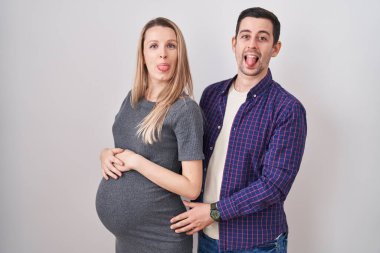 Genç bir çift beyaz arka planda duran bir bebek bekliyor. Komik bir ifadeyle dillerini dışarı çıkarıyorlar. duygu kavramı. 