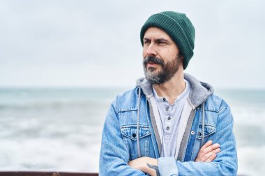 Kel genç adam sahilde kollarını kavuşturmuş el kol hareketi yapıyor.