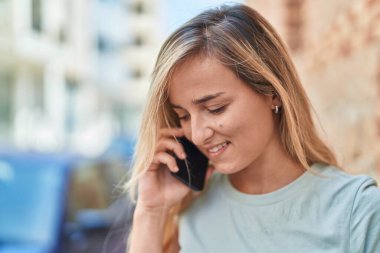 Genç sarışın kadın gülümsüyor. Kendine güveni tam. Akıllı telefondan konuşuyor.