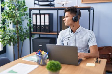 Ofiste çalışan, kulaklık takan, profil pozu veren, kendine güvenen gülümseyen genç İspanyol bir adam.. 