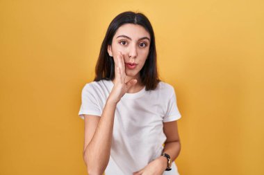 Sarı arka planda duran genç ve güzel bir kadın. Ağız üstünde el ele. Gizli dedikodular, kötü niyetli konuşmalar. 