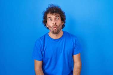 Mavi arka planda duran İspanyol genç adam dudaklarıyla balık suratı yapıyor, çılgınca ve komik bir jest. Komik ifade. 