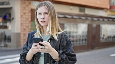 Kahve dükkanının terasında akıllı telefon kullanan genç sarışın kadın.